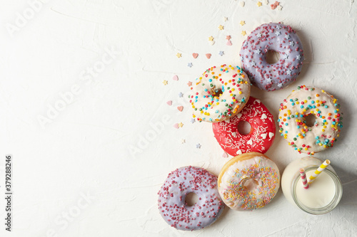 Milk and tasty donuts on white background, top view