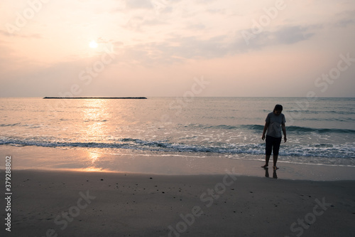 Tranquil scene of woman walking alone on the seaside and watching the sunset or sunrise.