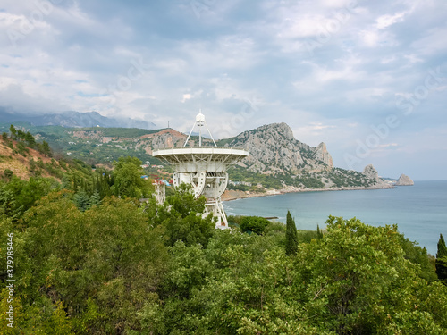 Antenna of radiotelescope among the trees on mountainous sea shore