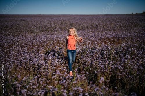 happy child, blond girl runs and jumps in violet flower field. Reconnection with nature.