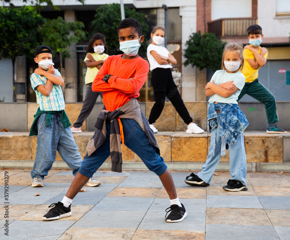 Modern tweens in protective face masks dancing hip-hop on summer street. New urban lifestyle concept during coronavirus. Conscious generation - obrazy, fototapety, plakaty 