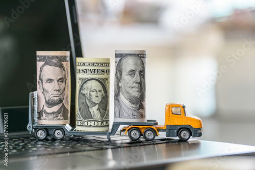 US USD 1, 5, 100 dollar bills, a trailer truck on a laptop computer, depicts wasting time and paying a lot of money to buy things online called online shopping or retail e-commerce, ecommerce concept photo