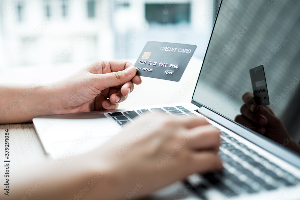The businesswoman's hand is holding a credit card and using a laptop for online shopping and internet payment in the office The businesswoman's hand is holding a credit card and using a laptop for online shopping and internet payment in the office