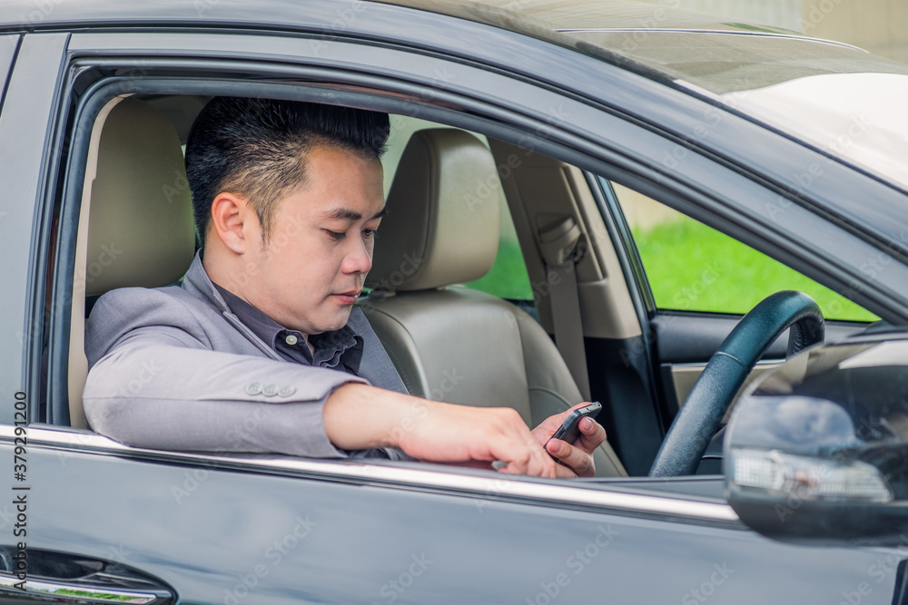 Happy businessman using smartphone calling while driving the car on his morning commute to work. Handsome Asian young man touching mobile phone communication on his luxury automobile on the road trip. Happy businessman using smartphone calling while driving the car on his morning commute to work. Handsome Asian young man touching mobile phone communication on his luxury automobile on the road trip.
