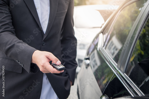 Businessman opens his luxurious car door with a modern remote control key. The young man is locking the automobile with the security system. Keyless in male hand. © Chaiyaphruek