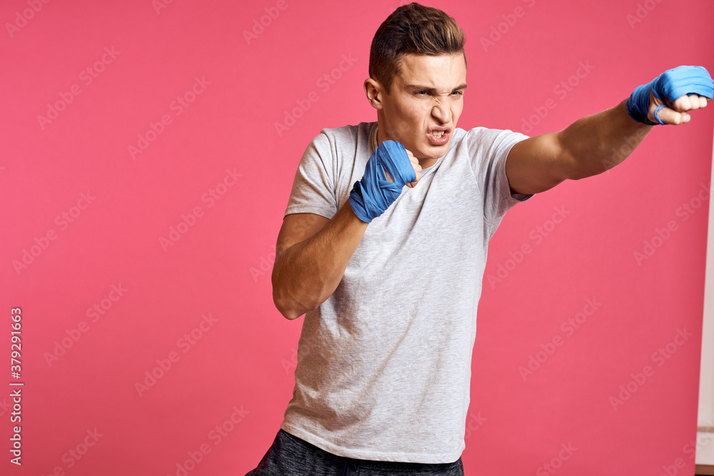 Sporty man in blue boxing gloves and a T-shirt on a pink background practicing punches cropped view