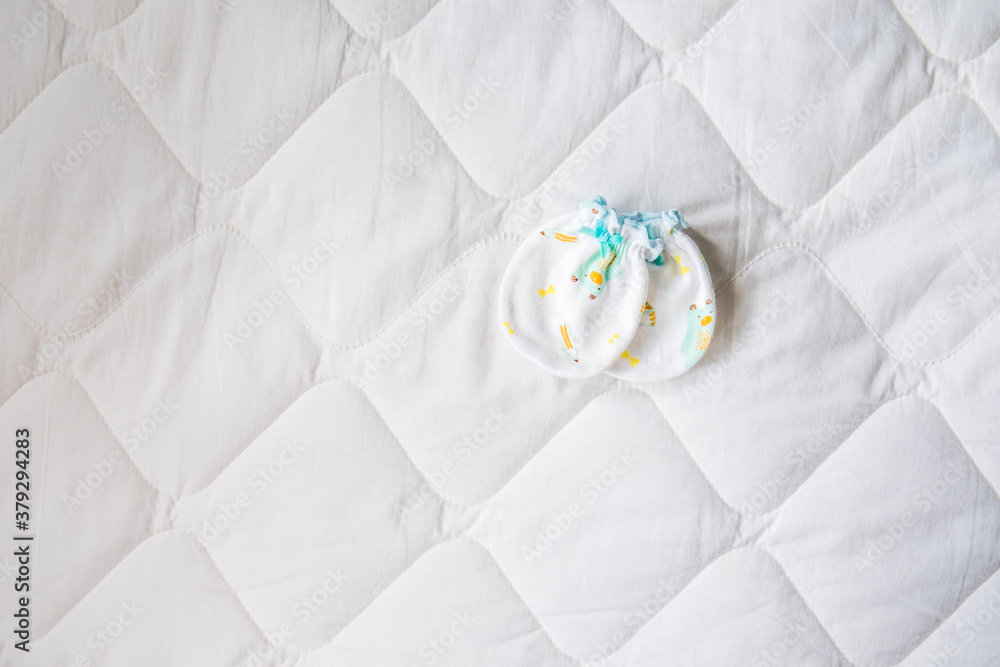 Above view of mittens for a newborn baby on a white blanket in the bedroom. Gloves for the infant put on the bed with copy space. Top-down Above view of mittens for a newborn baby on a white blanket in the bedroom. Gloves for the infant put on the bed with copy space. Top-down