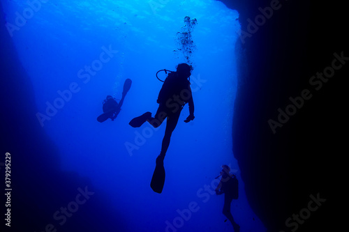 Scuba divers black silhouettes in a blue canyon making bubbles