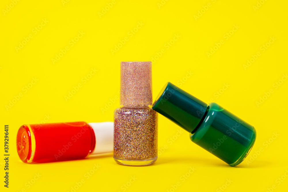 Close up three bottles with nail polishes of different colors, red, golden pink and dark green. Bright yellow background. Close up three bottles with nail polishes of different colors, red, golden pink and dark green. Bright yellow background.
