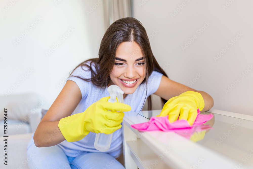 Beautiful young woman makes cleaning the house. Girl rubs dust. Smiling woman wearing rubber protective yellow gloves cleaning with rag and spray bottle detergent. Home, housekeeping concept. Beautiful young woman makes cleaning the house. Girl rubs dust. Smiling woman wearing rubber protective yellow gloves cleaning with rag and spray bottle detergent. Home, housekeeping concept.