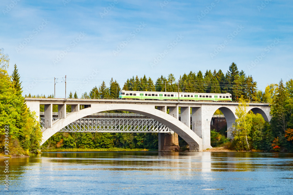 Autumn landscape of bridge with moving passenger train and Kymijoki river waters in Finland, Kouvola, Koria