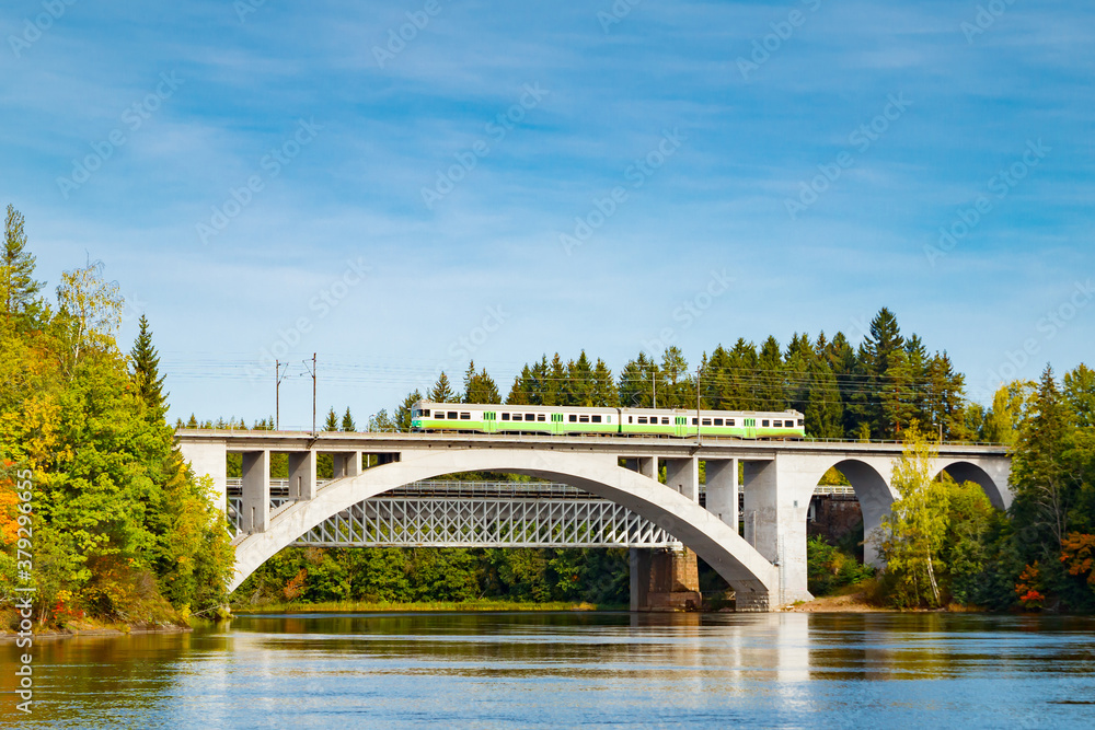 Autumn landscape of bridge with moving passenger train and Kymijoki river waters in Finland, Kouvola, Koria