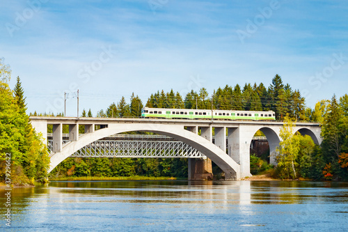 Autumn landscape of bridge with moving passenger train and Kymijoki river waters in Finland, Kouvola, Koria