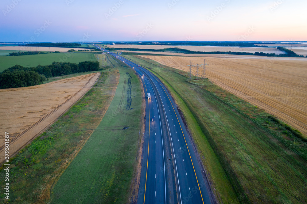 Highway along the wheat fields at dawn. Morning landscape from a height.