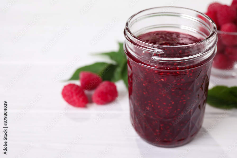Delicious jam in glass jar and fresh raspberries on white wooden table. Space for text Delicious jam in glass jar and fresh raspberries on white wooden table. Space for text