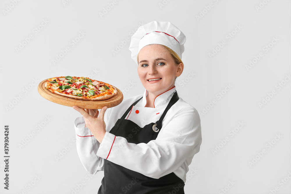 Mature female chef with tasty pizza on grey background