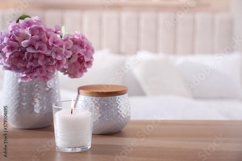 Burning candle and beautiful flowers on wooden table indoors. Space for text