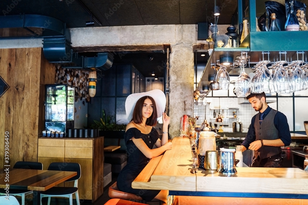 beautiful woman in black dress and a white wide-brimmed hat sitting at the bar in a cafe with a modern, trendy interior. Waiting for professional barista to prepare delicious, aromatic, fresh coffee beautiful woman in black dress and a white wide-brimmed hat sitting at the bar in a cafe with a modern, trendy interior. Waiting for professional barista to prepare delicious, aromatic, fresh coffee