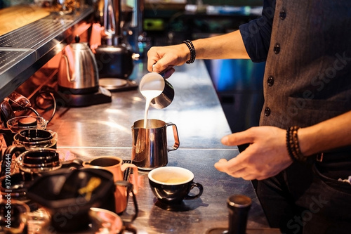 Close-up of barista hands pouring milk into coffee espresso  making cappuccino or latte. A professional barista preparing coffee with inspiration on the bar counter