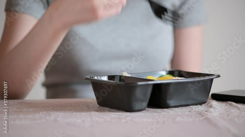 A woman puts a plastic container with a healthy salad on the table and eats. Female hands with fork close-up. Homemade ready meals delivered from a restaurant, ordered by phone. Diet, healthy snack.
