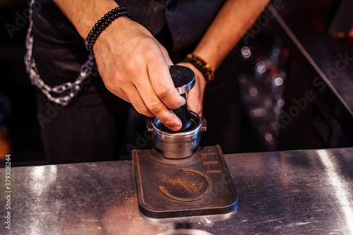 Close-up of the hands of a barista tamping ground coffee into the coffee machine. Professionally making Coffee Pack by temper in holder. Delicious coffee in an expensive high-class restaurant