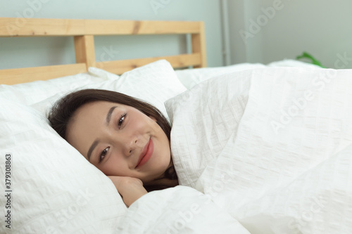 Asian women wake up happy and smile on white bed in bedroom.