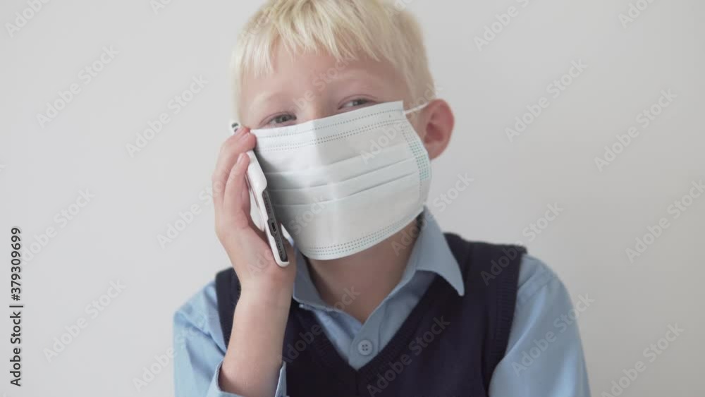 A boy in a medical mask is talking on a mobile phone.