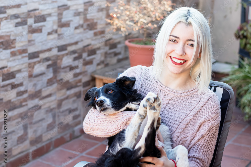 Blonde young woman hugging her dog while sitting outdoors in a terrace Blonde young woman hugging her dog while sitting outdoors in a terrace