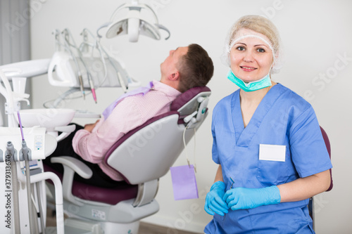 Portrait of qualified female stomatologist in dental clinic with patient in chair behind