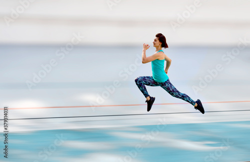 Sporty young woman running by all-season track at the city stadium.