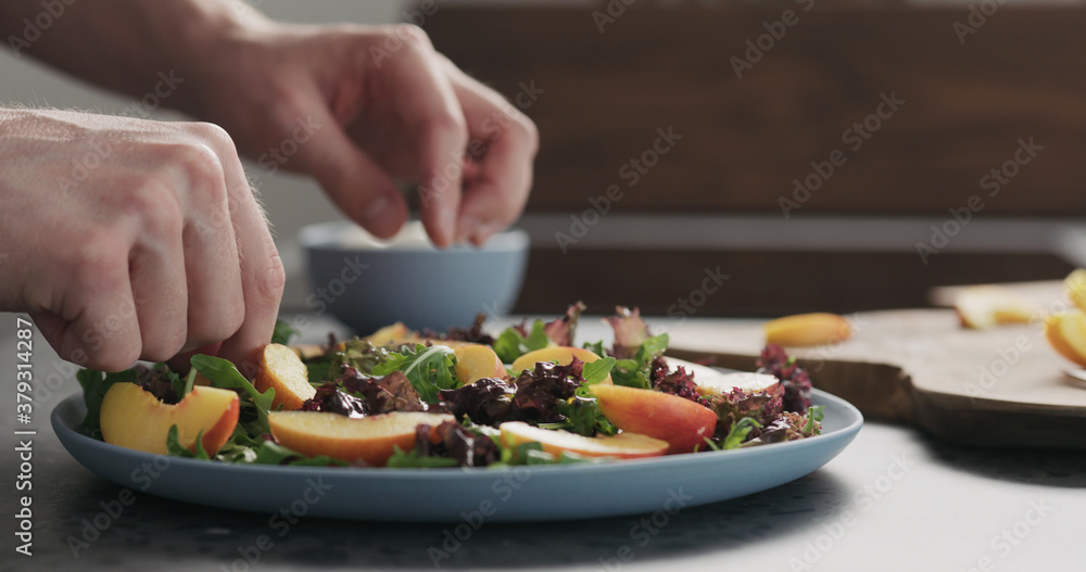 man making salad with nectarines and mozzarella on a blue plate on concrete countertop on kitchen, add nectarines