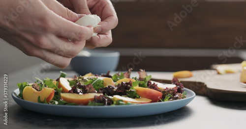 man making salad with nectarines and mozzarella on a blue plate on concrete countertop on kitchen, add mozzarella
