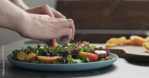 man making salad with nectarines and mozzarella on a blue plate on concrete countertop on kitchen, add nectarines