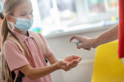Girl in preventive mask disinfecting her hands while enetering the school