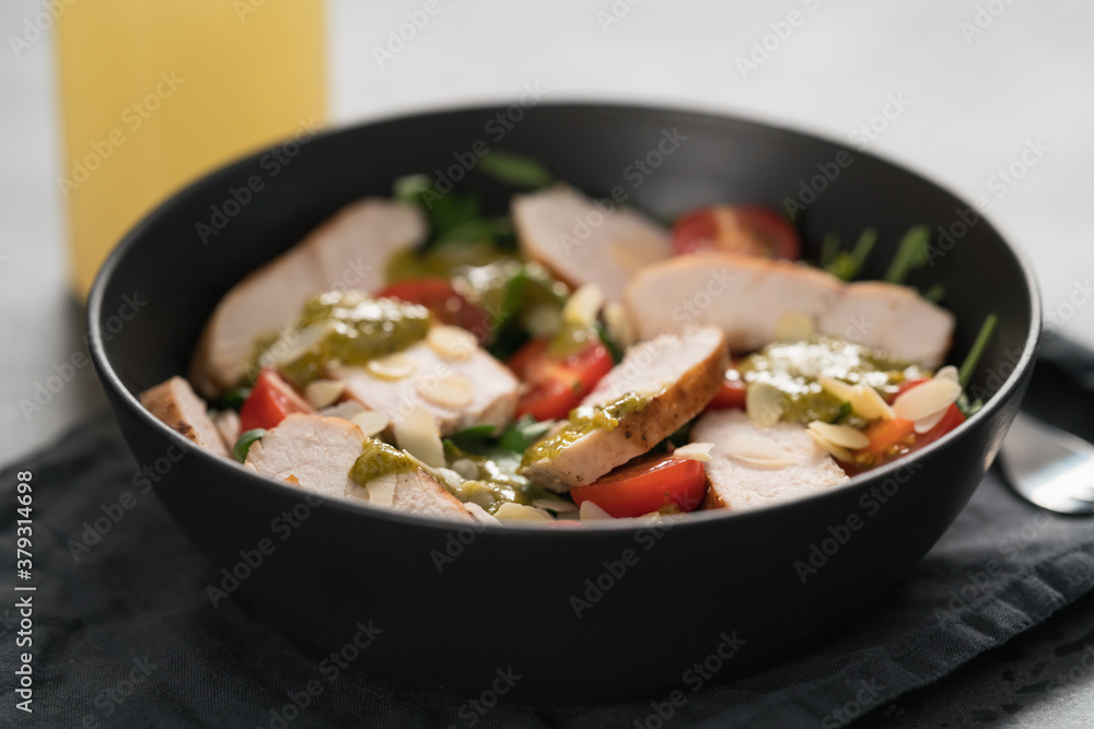 Salad with chicken, tomatoes, arugula and pesto in black bowl on concrete background Salad with chicken, tomatoes, arugula and pesto in black bowl on concrete background