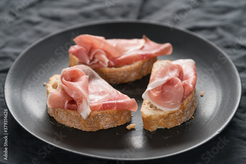 ciabatta with thin prosciutto on black plate on linen background