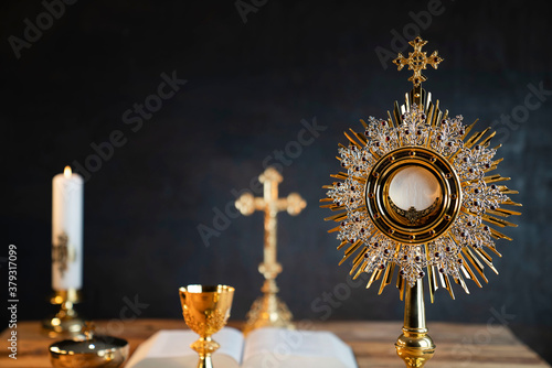 Catholic religion concept. Catholic symbols composition. The Cross, monstrance,  Holy Bible and golden chalice on wooden altar. 