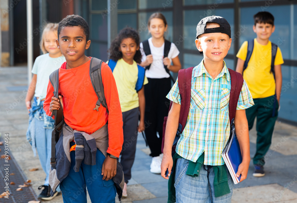 Obraz premium Group of schoolchildren with backpacks going together to open air lesson