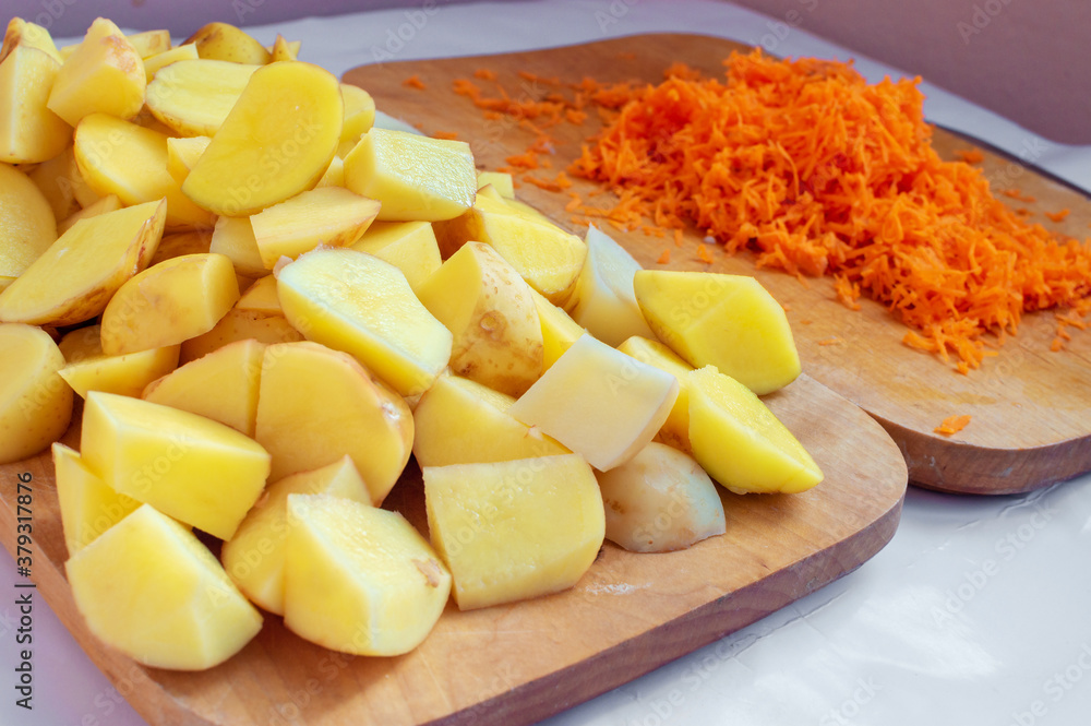 A pile of chopped potatoes and carrots are lying on cutting boards. Preparing vegetable ingredients for cooking A pile of chopped potatoes and carrots are lying on cutting boards. Preparing vegetable ingredients for cooking