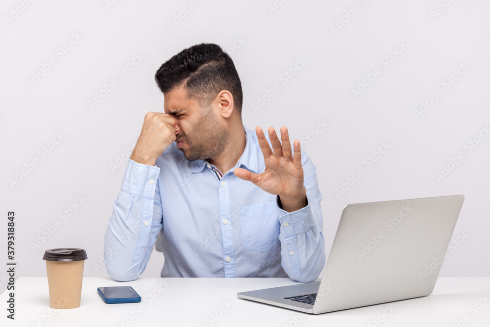 Displeased male employee confused by bad smell in office workplace, holding breath pinching his nose Displeased male employee confused by bad smell in office workplace, holding breath pinching his nose