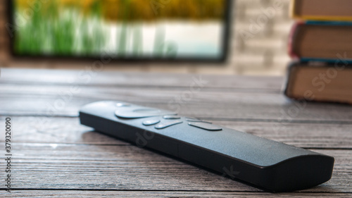 Modern TV remote control on the surface and TV on the wall in the background.