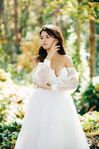 Beautiful bride in a white dress stands in the autumn forest.