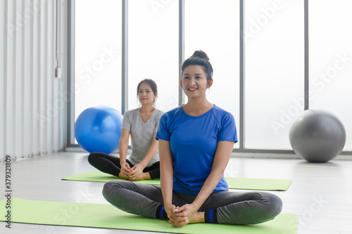 Two middle-aged Asian women doing yoga sitting on a rubber mat in a gym.