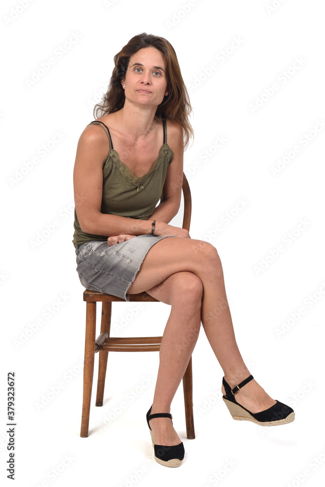 front view of a serious woman in denim skirt sitting on a chair and looking at camera on white background,legs crossed front view of a serious woman in denim skirt sitting on a chair and looking at camera on white background,legs crossed