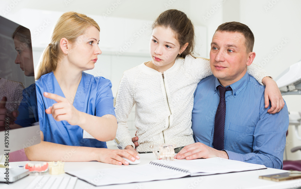 Obraz premium Female dentist explaining X-ray on computer to father with teenage girl at dental clinic
