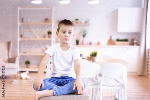 child in a white T-shirt and jeans sits on a chair