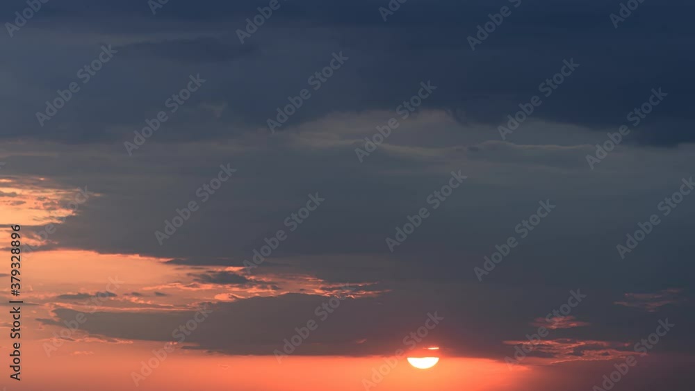 Time lapse of setting huge sun through the moving sunset clouds in rainy fiery orange sky Time lapse of setting huge sun through the moving sunset clouds in rainy fiery orange sky