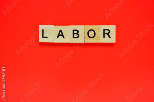 Word labor. Wooden blocks with lettering on top of red background. Top view of wooden blocks with letters on red surface