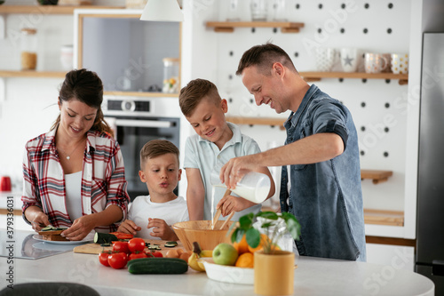 Mother and father making breakfast with sons. Young family preparing delicious food in kitchen.