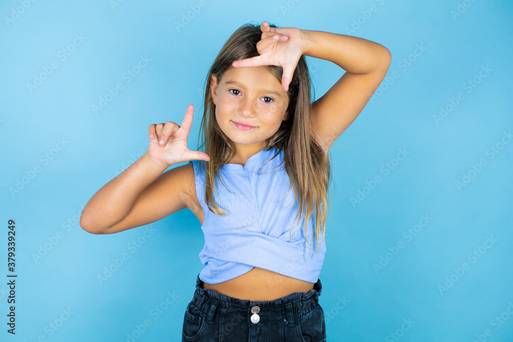 Young beautiful child girl over isolated blue background smiling making frame with hands and fingers with happy face Young beautiful child girl over isolated blue background smiling making frame with hands and fingers with happy face